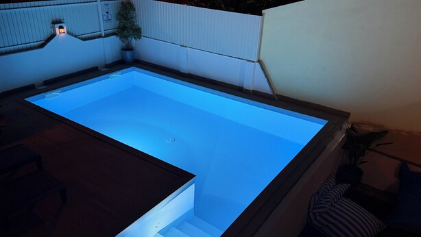 Une piscine rectangulaire à l’eau claire, entourée d’un mur blanc et d’une terrasse en bois.