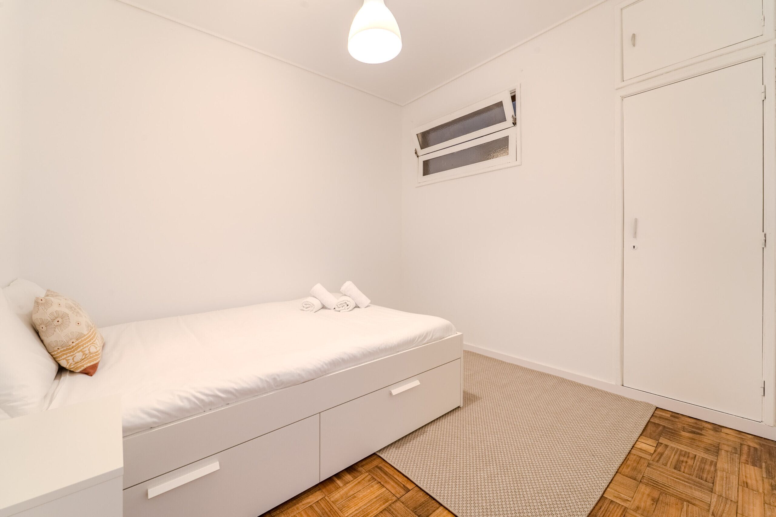 A bedroom with a bed, a wardrobe, a window, and a ceiling light.