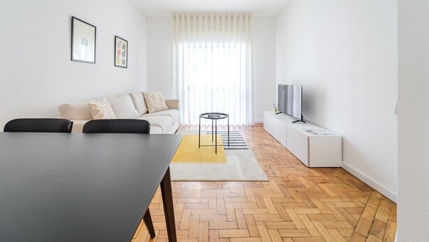 Ein modernes Wohnzimmer mit einer Couch, einem Couchtisch, einem Fernseher und einem Fischgrätparkettboden.