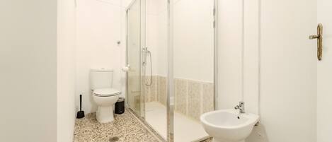A bathroom with a toilet, bidet, and glass-enclosed shower.
