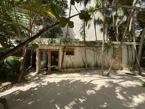 A sandy courtyard with a wooden door labeled 'FRONTDESK,' surrounded by tropical vegetation and a white wall. - Casa Chechén by Aldea Canzul (Tulum)