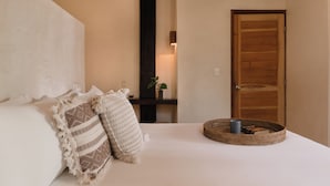 Une chambre à coucher avec un lit, des oreillers, une table de chevet ornée d’une plante et une porte en bois.
