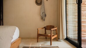 Une chambre à coucher avec un lit, une chaise en bois, un tapis à motifs et un chapeau accroché au mur.