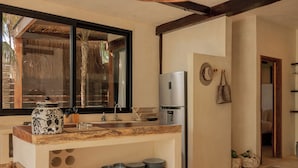 Une cuisine dotée d’un plan de travail en bois, d’un réfrigérateur en acier inoxydable et d’une fenêtre donnant sur une construction à toiture de chaume.