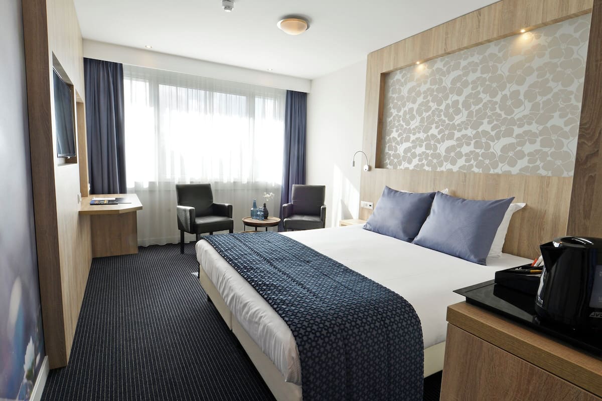 A hotel room with a large bed, a desk with a chair, a TV, and a coffee maker.