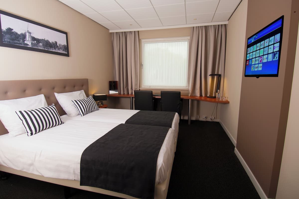 A hotel room with two beds, a desk, a chair, a TV, and a window with curtains.