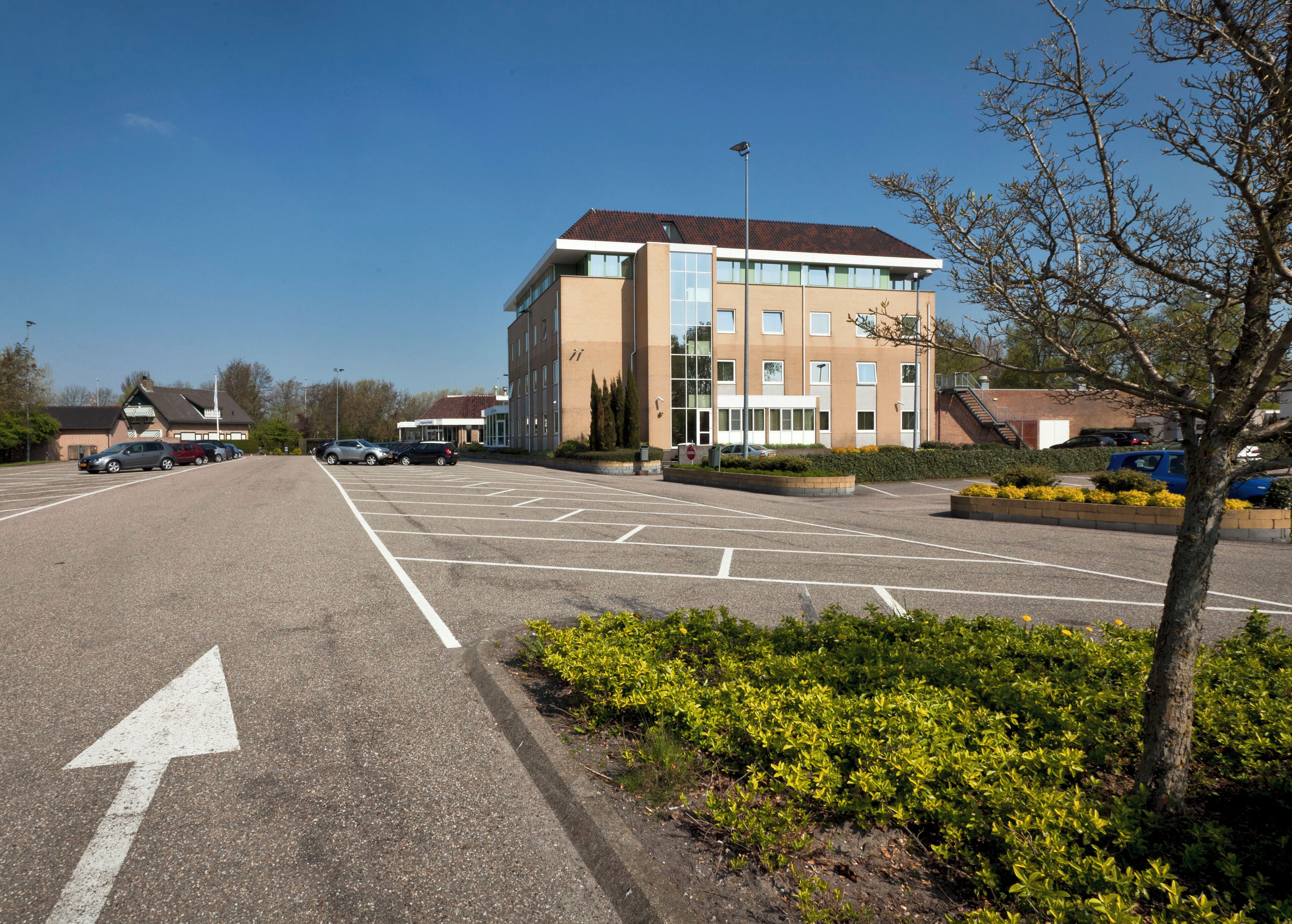 A parking lot with multiple cars, a building with a red roof, and a clear blue sky.