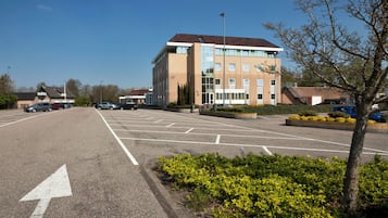 A parking lot with multiple cars, a building with a red roof, and a clear blue sky.