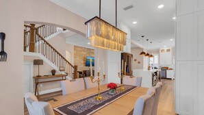 A spacious dining area with a long wooden table, white chairs, and a chandelier. - Ultimate Disney Experience PLUS MORE!  (Kissimmee)