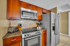 A kitchen with wooden cabinets, a stainless steel microwave, a refrigerator, a stove, and a tiled backsplash.