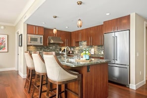 A modern kitchen with a central island, bar stools, stainless steel appliances, and pendant lighting.