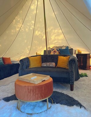 Ein Zeltinnenraum mit einer Couch, Kissen, einem Holztisch und einem flauschigen Teppich.