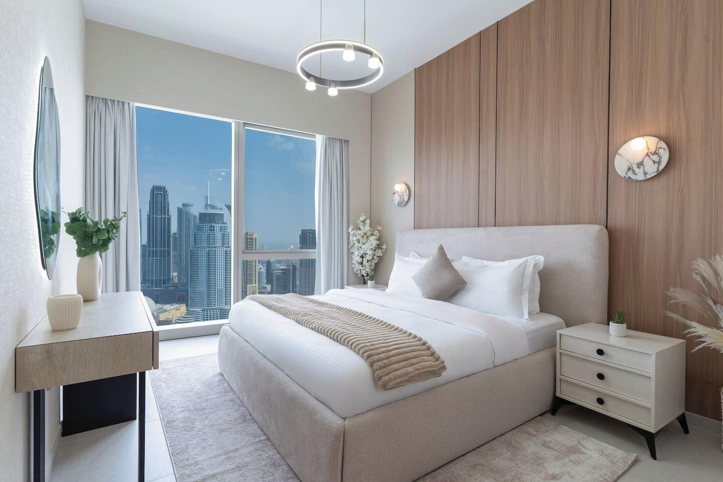 Une chambre moderne avec un grand lit, une table de chevet, une commode, un miroir et une vue sur le paysage urbain.