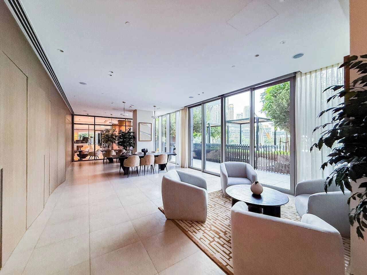Un espace salon spacieux et moderne, doté de sièges confortables, de grandes fenêtres offrant une vue sur la ville et d’un aménagement épuré et minimaliste.