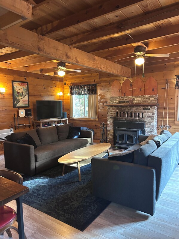 A cozy cabin interior with a wooden ceiling, a fireplace, a sofa, a television, and a dining area. - Quaint 1-bedroom cabin in Kyburz for a cozy getaway (Kyburz)