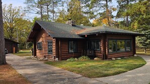 A log cabin with a porch, a mailbox, and a gravel driveway.