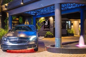A luxury car parked in front of a hotel entrance with a signboard, a water feature, and a tiled pathway. - Gigiri Lion Villas II (Nairobi)