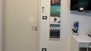 A hotel room with a white door, a mounted air conditioner, a flat-screen TV, a small potted plant, and a framed picture on the wall. - United Residence (Mestre)