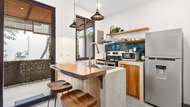 Una cocina moderna con una isla central, taburetes de bar, un refrigerador, un microondas y un fregadero.