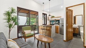 Una sala moderna con un sofá, un sillón verde, una mesa de centro de madera y un ventanal con vistas a zonas verdes.