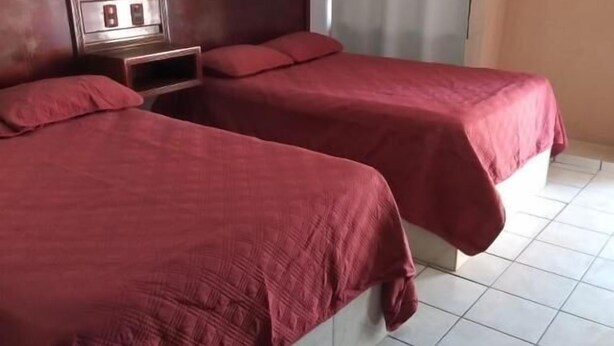 Une chambre d’hôtel avec deux lits, une tête de lit en bois, une table de chevet et une fenêtre avec des rideaux.