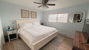 A bedroom with a bed, a nightstand, a dresser, a ceiling fan, a window, and two wall decorations.