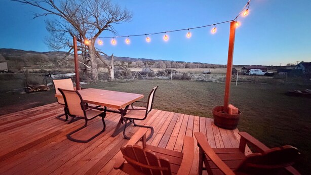 A wooden deck with a table and chairs, string lights, and a view of the countryside.