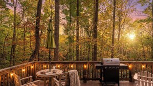 Une terrasse en bois avec un barbecue, des chaises, une table et des guirlandes lumineuses.