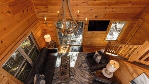 L’intérieur d’un chalet en bois chaleureux et accueillant, avec un canapé en cuir noir, un lustre et une grande fenêtre donnant sur le paysage extérieur.