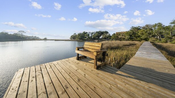 Een houten steiger die uitkomt bij een rustig meer, met een bankje en een pad.