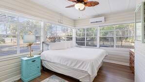 Een slaapkamer met een bed, een plafondventilator, een raam met jaloezieën, een nachtkastje en een dressoir.