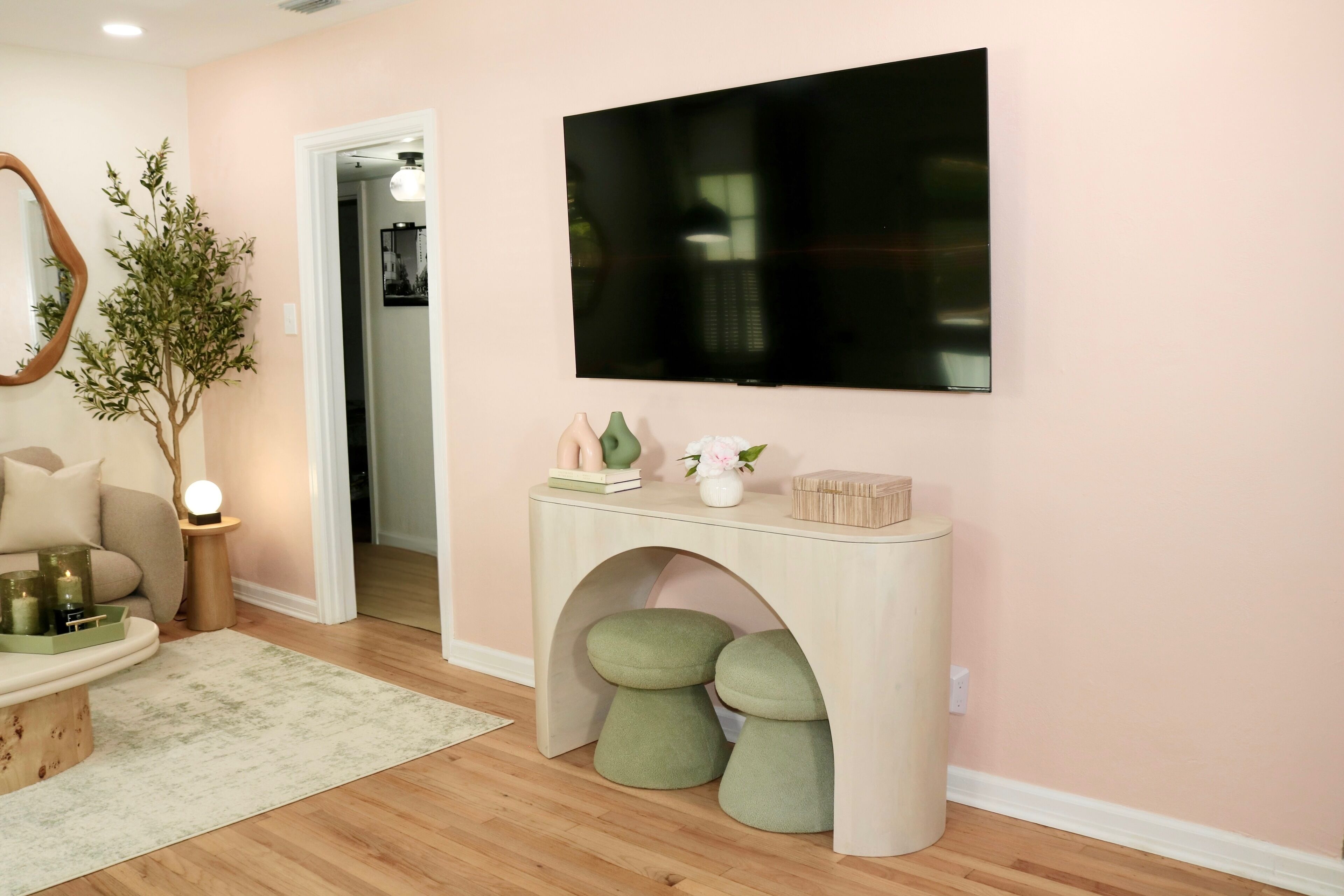 Ein Wohnzimmer mit an der Wand montiertem Fernseher, einem Konsolentisch mit Dekoration, einer Pflanze und einer gemütlichen Sitzecke.