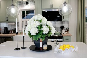 Een moderne keuken met een centraal eiland, een witte hortensia in pot, een kandelaar en een schaal met citroenen.