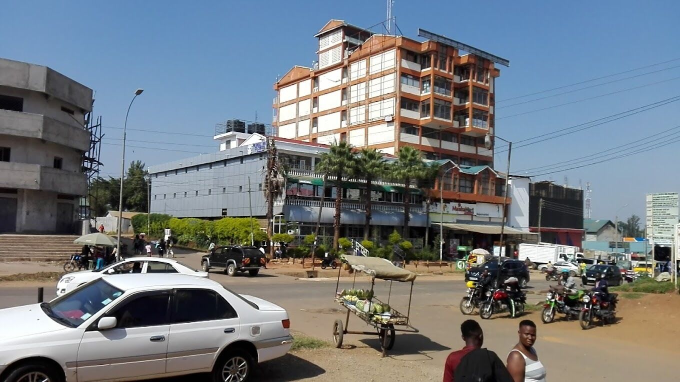 A busy street with a white car parked on the side, a building with multiple floors, and several motorcycles and cars in the background.