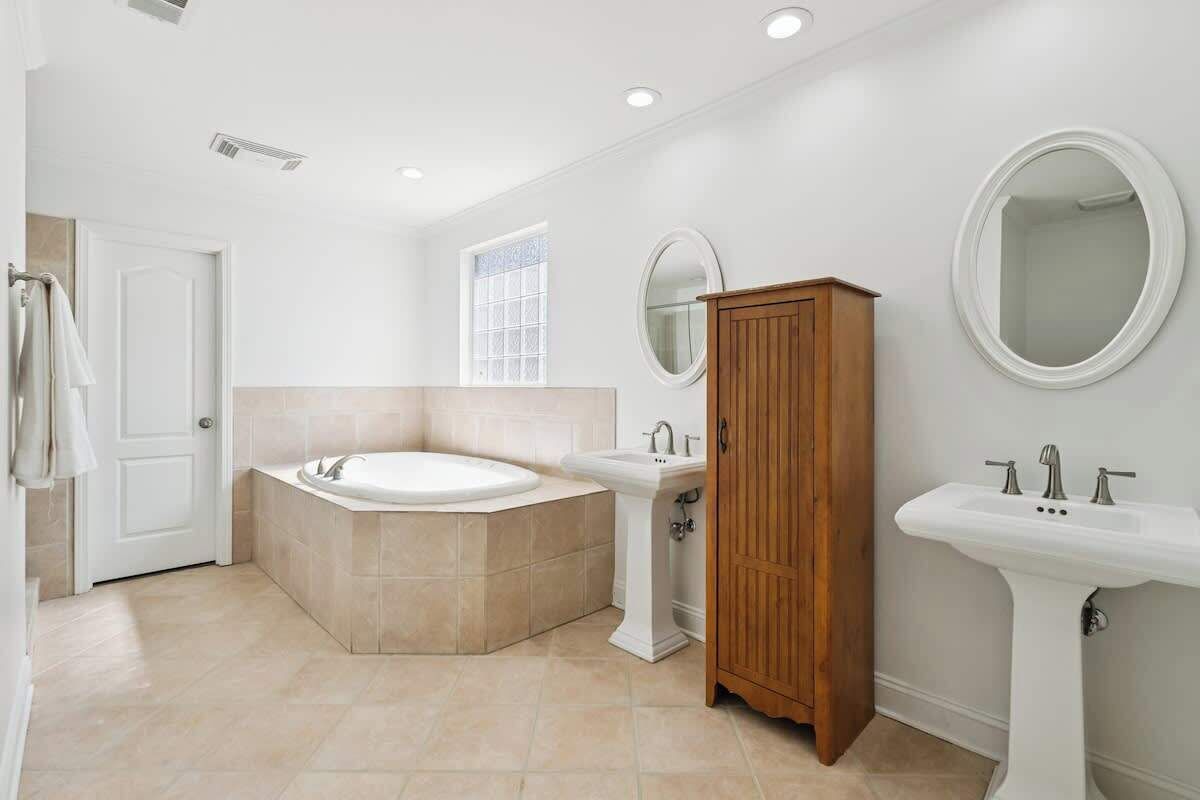 Un baño moderno con bañera, lavamanos pedestal, armario de madera y espejo redondo.