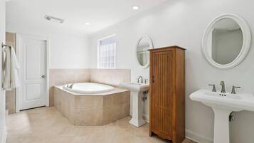 Un baño moderno con bañera, lavamanos pedestal, armario de madera y espejo redondo.