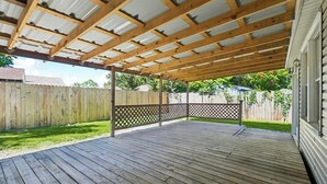 Une terrasse en bois couverte, dotée d’une clôture en treillis, d’une balustrade en bois et d’un toit en métal.