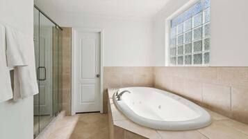 Un bagno con una vasca freestanding, cabina doccia in vetro e finestra con vetro smerigliato.