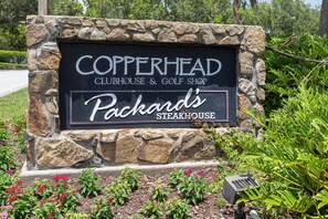 Segnaletica per Copperhead Clubhouse & Golf Shop e Packard's Steakhouse, circondata da muri in pietra e piante fiorite.