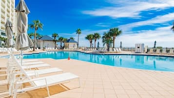 A pool area with lounge chairs, umbrellas, and palm trees.