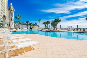 A pool area with lounge chairs, umbrellas, and palm trees.