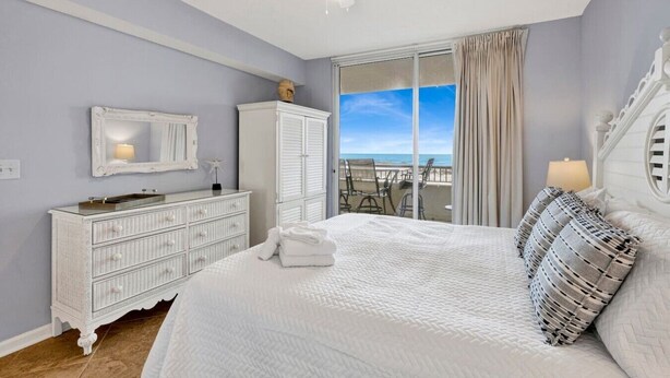 Ein Schlafzimmer mit Bett, Kommode, Spiegel und Blick auf den Strand.