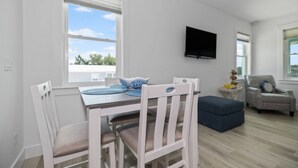 A dining area with a table and chairs, a television mounted on the wall, and a view of the outdoors through a window.