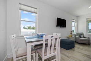 Un comedor con una mesa y sillas, un televisor montado en la pared y vistas al exterior a través de una ventana.