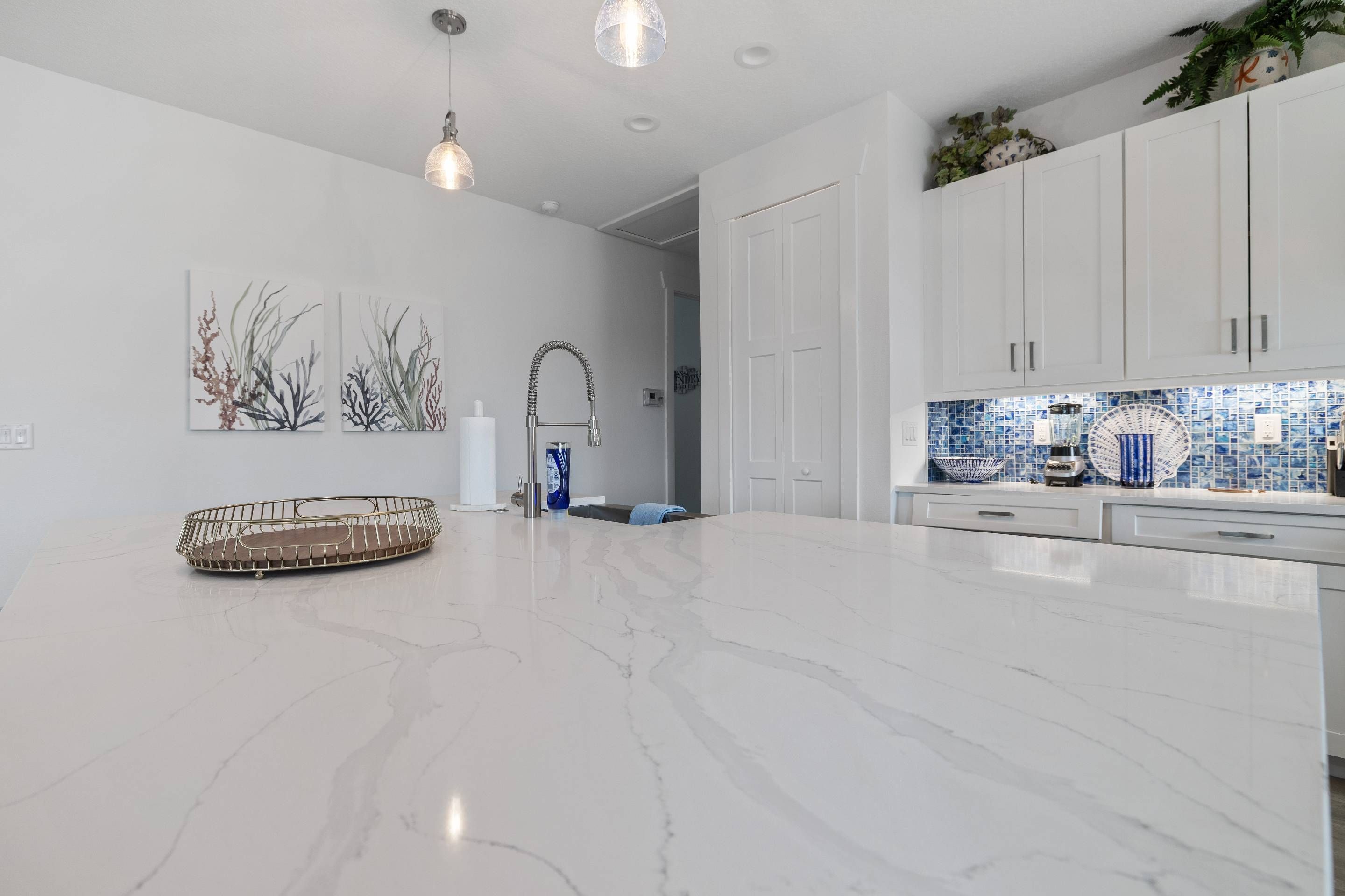 Uma cozinha moderna com armários brancos, bancada de mármore e mosaico azul na parede.