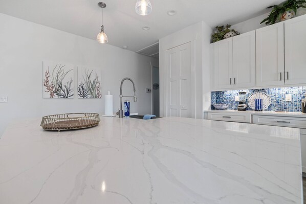 A modern kitchen with white cabinetry, a marble countertop, and a blue mosaic backsplash.