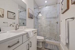 Un baño moderno con ducha de mampara de vidrio, un lavamanos blanco y un inodoro.