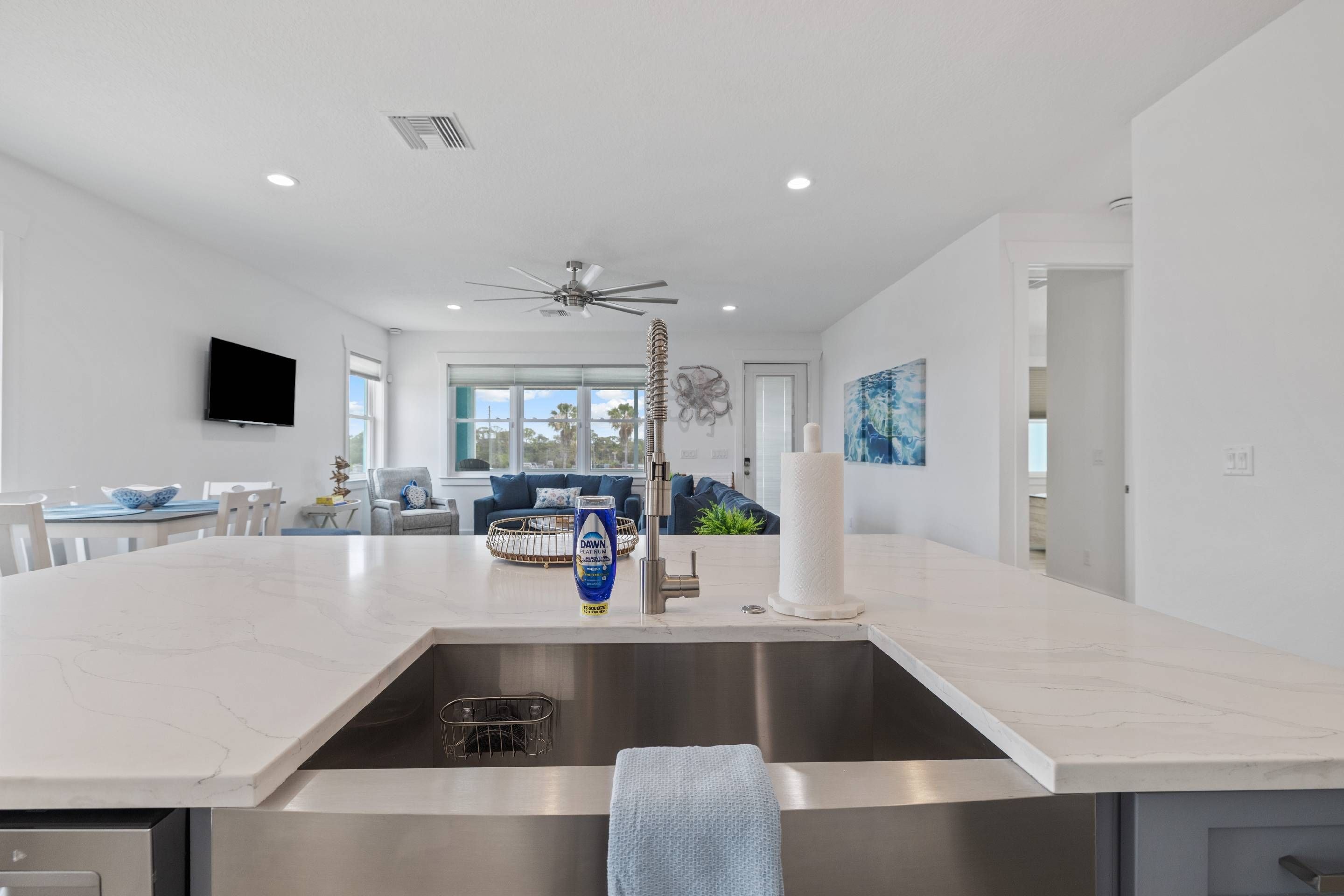 A modern kitchen with a central island, stainless steel sink, and a ceiling fan.