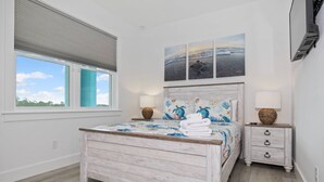 A bedroom with a bed, a nightstand, a lamp, a window, and artwork on the wall.