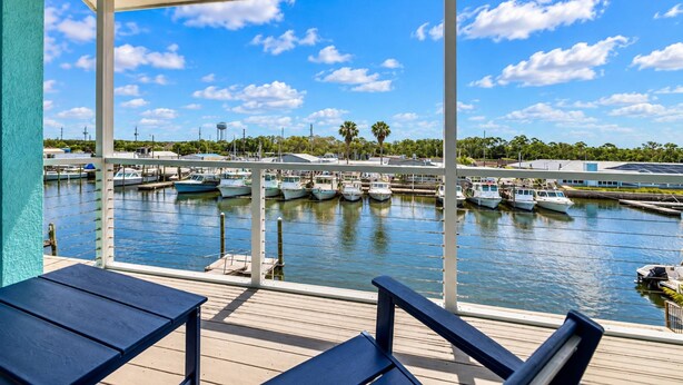 A view from a covered deck overlooking a marina with boats docked, a clear sky, and a water tower in the background.